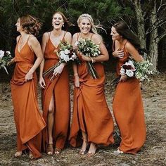 bridesmaids in orange dresses laughing and holding bouquets with trees in the background