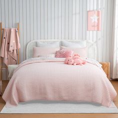 a bed with pink comforter and pillows in a girls's bedroom, next to a teddy bear