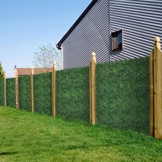 a green fence with wooden posts in front of a house and grass area next to it