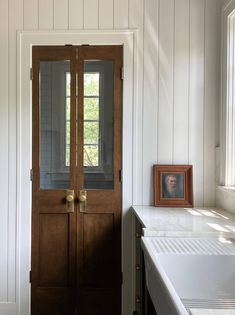 a wooden door in a white kitchen next to a counter with a framed photo on it