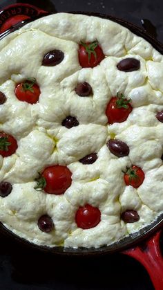 a pizza with olives, tomatoes and cheese in a pan on a stove top