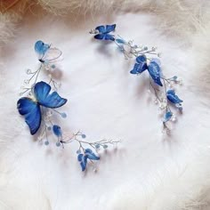 two blue butterflies on white feathers with beads and leaves attached to the back of their wings