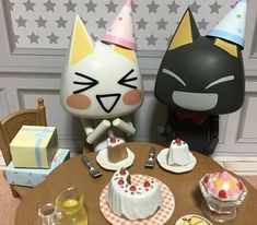 two cat figurines sitting on top of a table next to cakes and cupcakes