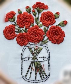 red flowers are in a mason jar embroidered onto a white piece of cloth that is stitched together