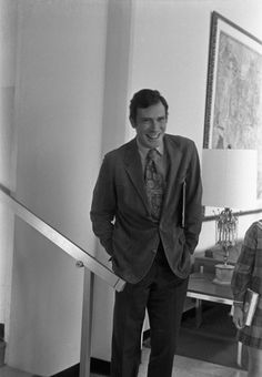 a man in a suit and tie standing at the bottom of a stair case with his hands in his pockets