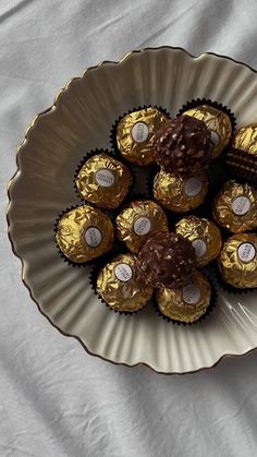 chocolates are arranged in a bowl on a white tablecloth with gold trimming