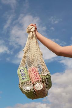 a person holding a mesh bag full of bottles in the air with clouds in the background