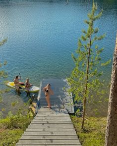 two people on surfboards are at the end of a dock with a boat in the water