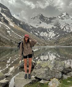 a woman is standing on rocks near the water with mountains in the backgroud