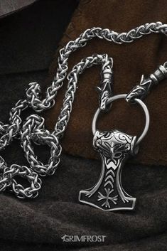 Vikings used necklaces with animals or beasts biting onto a ring where pendants were hung. This variant consists of a thick Stainless Steel chain ending in Geri and Freki, the wolves of Odin, that bite onto a pendant ring with a Stainless Steel Thor's Hammer depicting the mask of Odin and the Helm of Awe symbol. #viking #vikings #jewelry #grimfrost Viking Style Engraved Metal Necklaces, Gothic Jewelry Chain Pendant, Gothic Pendant Chain Jewelry, Gothic Pendant Jewelry With Chain, Gothic Jewelry Pendant Chain, Silver Viking Style Metal Necklace, Symbolic Round Pendant Chain Jewelry, Viking Style Metal Round Pendant Jewelry, Viking Style Stainless Steel Pendant Necklace