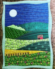 a quilted wall hanging on the side of a bed with a house and mountains in the background