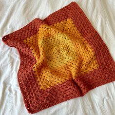 an orange and yellow crocheted blanket laying on top of a white bed sheet