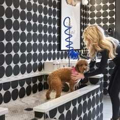 a woman is petting a small dog in a bathroom with black and white wallpaper