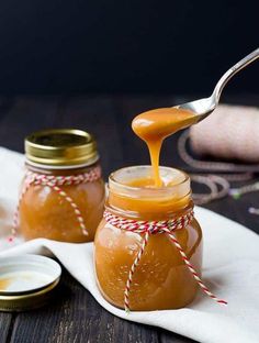 a spoon full of honey sitting on top of a wooden table next to two jars