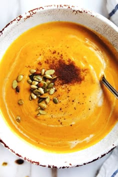 a white bowl filled with carrot soup and topped with pumpkin seeds, cinnamon sprinkled on top