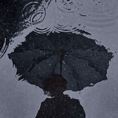 the reflection of a person holding an umbrella is shown in the water on a rainy day