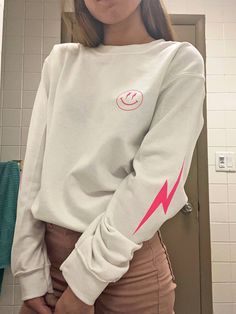 Bring happiness wherever you go with this super trendy lightning bolt smiley face crewneck sweatshirt! Featuring a bold, simple, smiley face graphic in hot pink and lightning bolts on each sleeve, this piece is perfect to finish off your trendy, oversized look! It is preppy, and adorable! Makes a great gift for a friend, or for yourself! Please note: This item features heat transferred plastisol graphics. Printed on a soft, cotton-poly blend Gildan sweatshirt. SIZING: Our sweatshirts are unisex Trendy Relaxed Fit Sweatshirt, Trendy Crew Neck Sweatshirt, Trendy White Crew Sweatshirt, Trendy Everyday Crew Neck Sweatshirt, Winter Smiley Face Crew Neck Sweatshirt, Trendy White Everyday Sweatshirt, Casual Smiley Face Winter Sweatshirt, Cool Long Sleeve Relaxed Fit Tops, Casual Winter Sweatshirt With Smiley Face