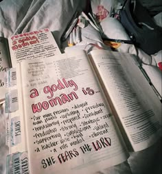 an open bible laying on top of a bed next to other books and writing utensils