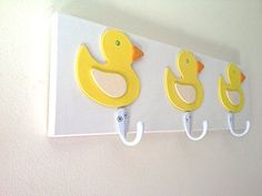 three yellow rubber ducks hang from hooks on a white wall in a children's room