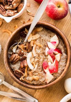 a bowl of oatmeal topped with apples and pecans next to spoons