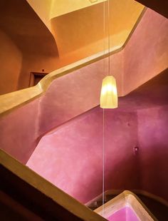 a light hanging from the ceiling in a room with pink walls and stairs, next to a window