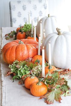 a table topped with lots of white pumpkins and greenery on top of it