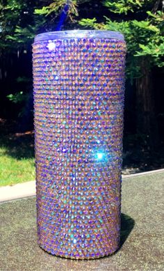 a purple trash can sitting on top of a cement ground next to a green tree