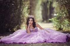 a woman in a purple dress laying on the ground wearing a tiara and posing for a photo