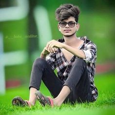 a young man sitting in the grass wearing glasses