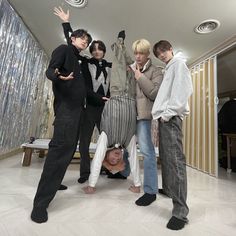 four young men standing in a room with one laying on the floor and another lying down