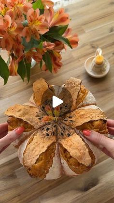 a person holding a piece of bread in their hands with flowers on the table behind them