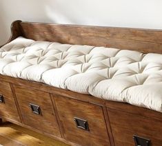 a wooden bench with white cushions on it's seat and two drawers in the back