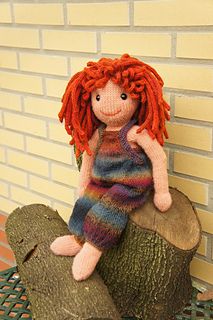 a red haired doll sitting on top of a tree stump in front of a brick wall