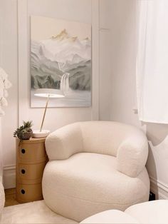 a white chair sitting in front of a painting on the wall next to a dresser