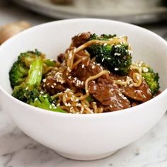 a white bowl filled with beef and broccoli on top of a marble counter