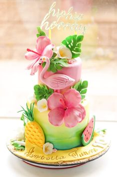 a three tiered cake with pink flowers and flamingos on top, sitting on a plate