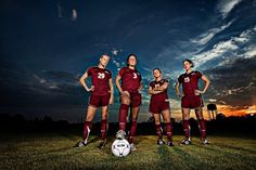 three girls in maroon uniforms standing next to a soccer ball on the field at sunset