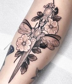 a black and white tattoo with flowers on the arm, holding a knife in it's hand