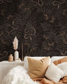 a white bed topped with lots of pillows next to a wall covered in black and brown wallpaper