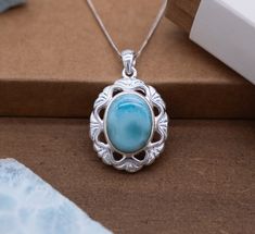 Adorn yourself with the ethereal beauty of nature embodied in our Silver Flower Pendant. This exquisite piece features a captivating oval Larimar stone nestled within an intricately crafted silver frame, reminiscent of a blooming flower in full splendor. Oval Larimar Center Stone: At the heart of this enchanting pendant lies a mesmerizing oval Larimar stone, exuding the serene blue hues and captivating patterns characteristic of this rare gem. The stone serves as the focal point, drawing the eye with its natural allure. Oval Silver Frame with Cut-Out Triangle Shapes: Surrounding the oval Larimar stone is a delicate silver frame meticulously fashioned into the shape of a flower. The frame is adorned with charming cut-out triangle shapes, enhancing the pendant's floral motif and adding depth Larimar Cabochon Jewelry Gift, Oval Blue Larimar Jewelry, Round Larimar Jewelry Gift, Round Larimar Jewelry For Gifts, Teardrop Larimar Jewelry Gift, Turquoise Oval Cabochon Jewelry For Gifts, Gift Necklaces With Oval Cabochon Natural Stones, Oval Cabochon Necklaces With Natural Stones For Gifts, Oval Larimar Jewelry For Anniversary