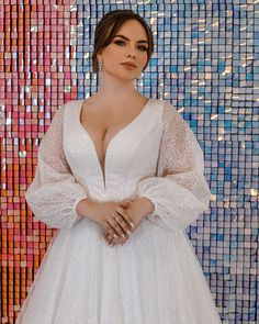 a woman standing in front of a colorful wall wearing a white dress with long sleeves