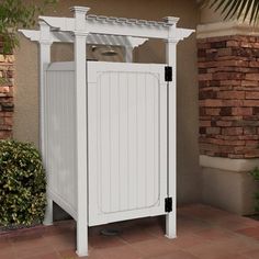 a white outdoor storage cabinet next to a brick wall and planter in front of a house