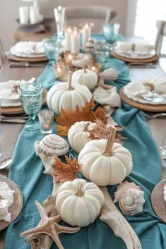 the table is set with white pumpkins and seashells