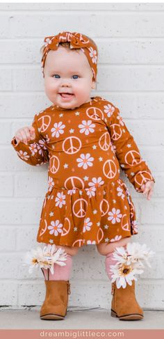 little girl wearing a fall dress that's brown with pink peace symbols and white daisies all over it. She's wearing brown boots with pink socks and white daisies in her shoes. Wearing a matching hair bow. Fitted Printed Tops For Playwear, Playful Long Sleeve Printed Dress, Spring Beachwear Tops For Play, Summer Long Sleeve Dress With All Over Print, Long Sleeve Printed Loungewear Dress, Fall Fashion Kids, Kids Fall Clothes, Infant Outfits, Kids Fall Outfits