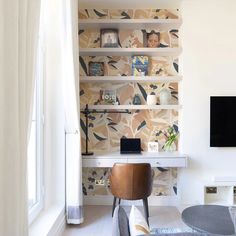 a living room with a tv, desk and shelves on the wall next to a window