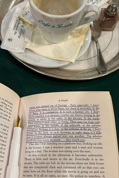 an open book on a table next to a cup of coffee and a pen with writing on it