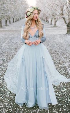 a woman wearing a blue dress and flower crown standing in the middle of an apple orchard