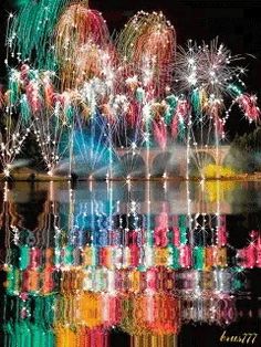 fireworks are lit up in the night sky over water and reflecting them on the surface