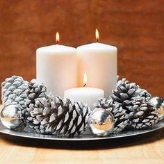 two white candles sitting on top of a metal tray with pine cones and silver balls