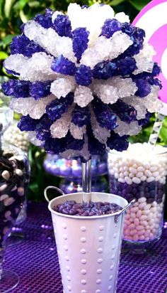 a purple and white centerpiece in a bucket on a table with other candy items